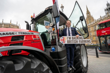 Gareth Davies MP on a tractor outside of the Palace of Westminster holding a sign reading "I'm backing British farming"